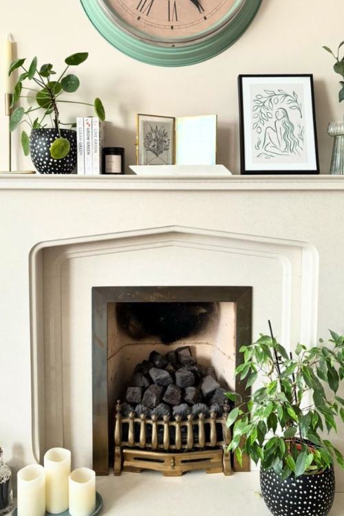 white fireplace with framed drawings and potted plants on mantel